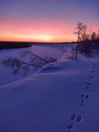 Snow covered landscape against sky during sunset