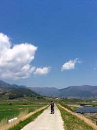 Rear view of boy riding bicycle on country road against sky
