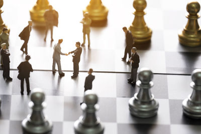 Business miniature hand shaking with chess on chessboard