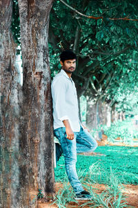 Portrait of young man standing against tree trunk