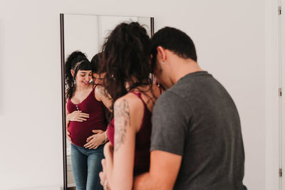 Smiling pregnant woman standing with male partner against mirror at home