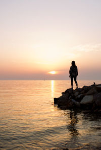 Woman silhouette standing on rock by the sea