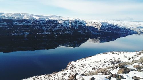 Scenic view of lake by snowcapped mountains against sky