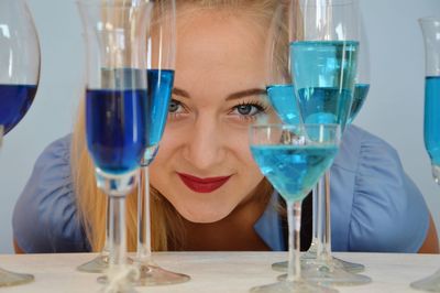 Portrait of young woman looking through drinks on table against blue background