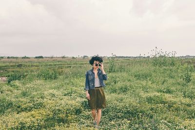 Portrait of mid adult woman wearing sunglasses standing on grassy field against sky