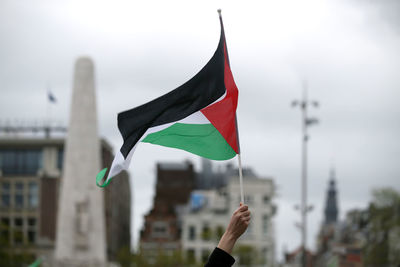 Cropped image of hand holding flag against sky