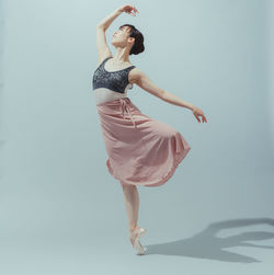 Full length of ballet dancer performing against gray background