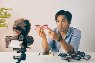 Portrait of boy holding camera while sitting on table