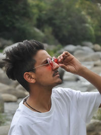 Side view of a indian young guy adjusting his sunglasses while standing outdoor with looking up