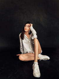 Portrait of young woman sitting against black background