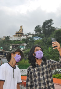 Two male friends with wearing face mask taking selfie together in outside during covid-19 pandemic 