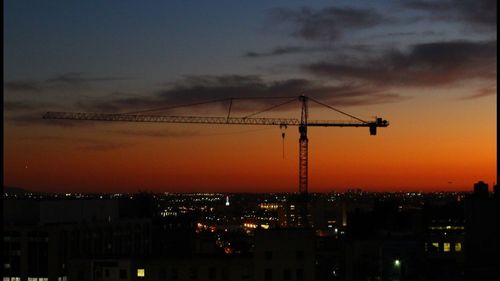 Silhouette cranes in city against sky at sunset