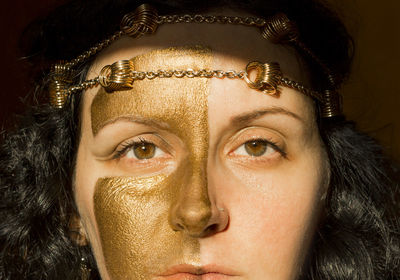 Portrait of a woman with gold make up on her face, half painted face, close up