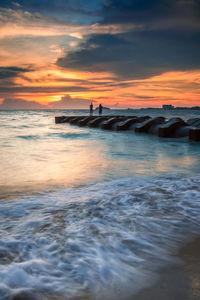 Silhouette of people standing on drainage pip in the sea at sunset