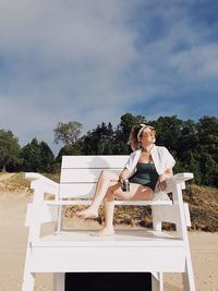 Young woman sitting on tree against sky