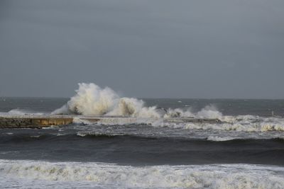 Waves splashing on shore against clear sky