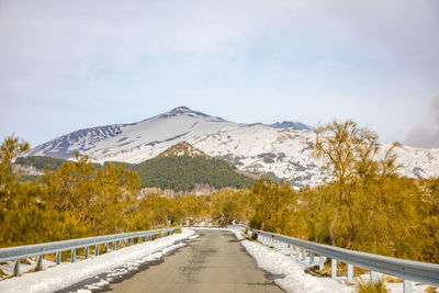 Road leading towards snowcapped mountains against sky