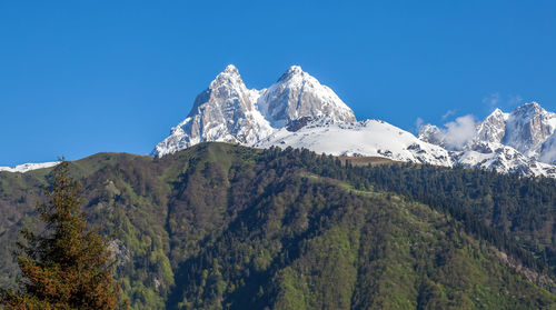 Low angle view of snowcapped mountains against clear blue sky