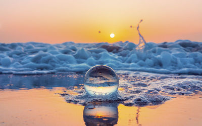 Close-up of snow on land against sea during sunset