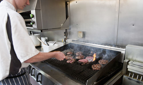 Chef flipping burgers on barbeque at restaurant kitchen