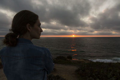 Woman looking at sea against sky during sunset