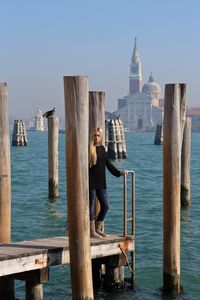 Young woman standing on pier over grand canal against sky with san marco campanile in background