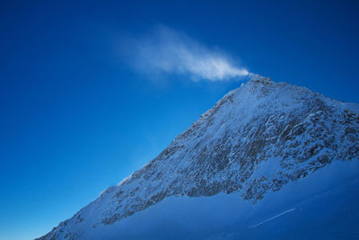 Low angle view of snowcapped mountain against blue sky