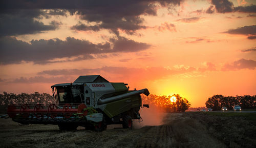 Combine harvester on field against sky at farm during sunset
