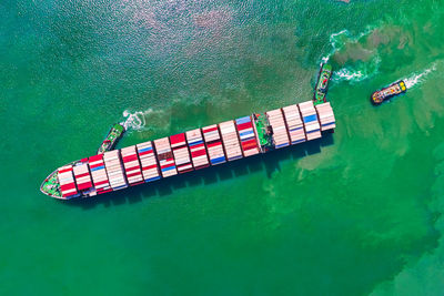 Container ship sailing in green sea and tugboat drag shipping to seaport.