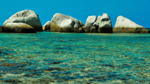 Rock formations in sea against clear blue sky