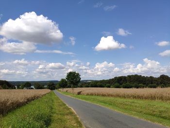 Empty road amidst field against sky