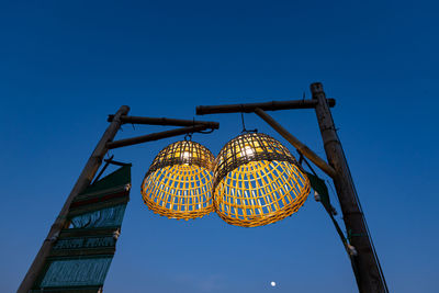 Low angle view of illuminated lighting equipment against clear blue sky