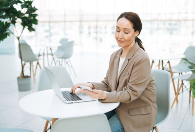 Adult business woman in stylish beige suit and jeans working on laptop at the public place