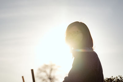 Low angle view of woman against bright sun during sunset