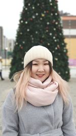 Portrait of smiling young woman standing against christmas tree