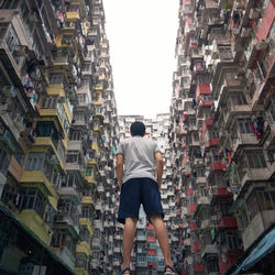 Rear view of man standing amidst buildings in city