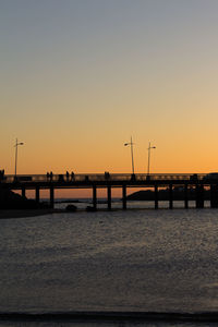Silhouette bridge over sea against clear sky during sunset