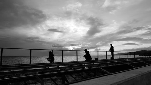 Silhouette people standing by railing against sky during sunset