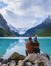 Rear view of woman sitting on rock by lake against mountain