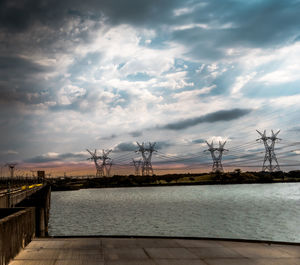 Cranes by sea against sky during sunset