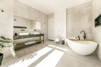 Modern interior of bathroom with white bathtub and ceramic wall mounted toilet and double sinks in minimal style