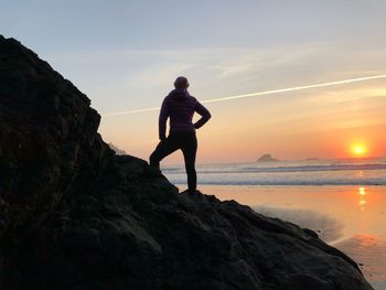 Silhouette woman standing on rock at beach against sky during sunset