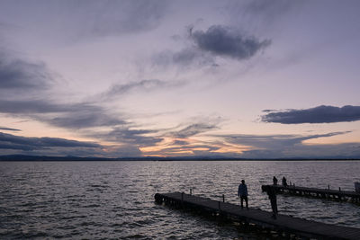 Silhouette people standing on pier by sea against sky during sunset