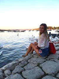 Young woman sitting on rock against sky