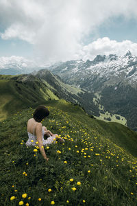 Woman sitting by flowering plants on mountains against sky