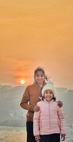 Portrait of young woman standing against sea during sunset