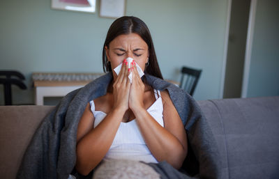 Woman sneezing while sitting by sofa at home