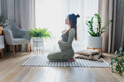Pregnant female doing prenatal yoga at home in the brightly living room
