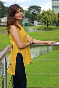 Side view portrait of young woman standing by railing at park