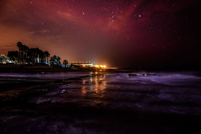 Illuminated beach against sky at night